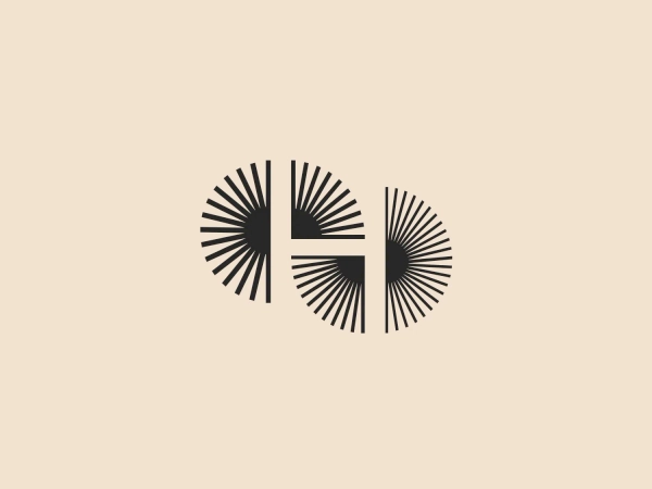The Houston Ballet logo depicts two stylized circular forms, reminiscent of abstract suns or flowers, with radial lines spreading outward from the centers. Each circle contains a solid block shape that cuts through the lines, creating a negative space effect. The design uses a monochromatic scheme with a dark gray or black color that provides a strong contrast, giving it a sleek, modern feel. The use of geometric symmetry and negative space creates a visually intriguing image that is both minimalistic and sophisticated.