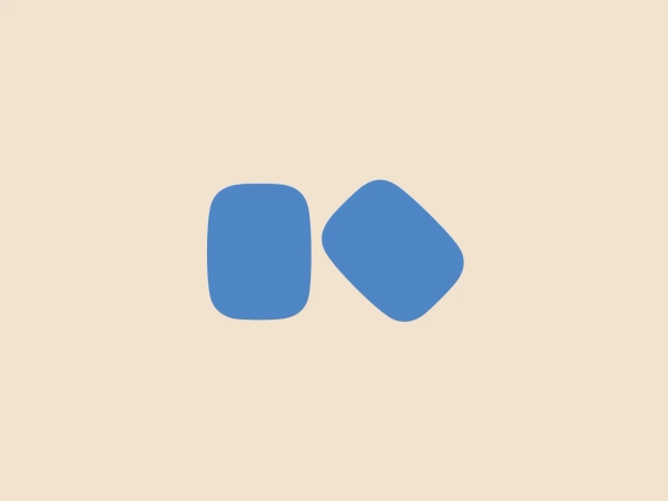The Kosé Corporation logo consists of two rounded geometric shapes—a square and a parallelogram—leaning against each other. Both shapes have soft, rounded corners and are a medium shade of blue, creating a professional and modern aesthetic. The orientation of the shapes gives a sense of movement or interaction. The simplicity of the design suggests versatility, representing various concepts from technology to partnership. The logo would complement a subtle and light background well.