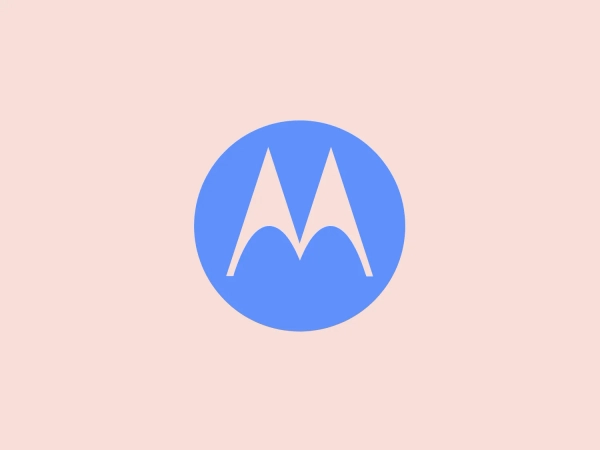 The Motorola logo features a stylized letter 'M' in bright white, set against a circular vibrant blue backdrop. The 'M' has a modern geometric design with pointed vertices at the top and a wave-like link between the two legs of the letter at the bottom, resembling mountain peaks. The contrast and simplicity of the design give it a clean, crisp, and easily recognizable aesthetic. A light, neutral shade such as pale pinkish-tan is a suitable background color that complements its vibrant tone while ensuring the white 'M' stands out.