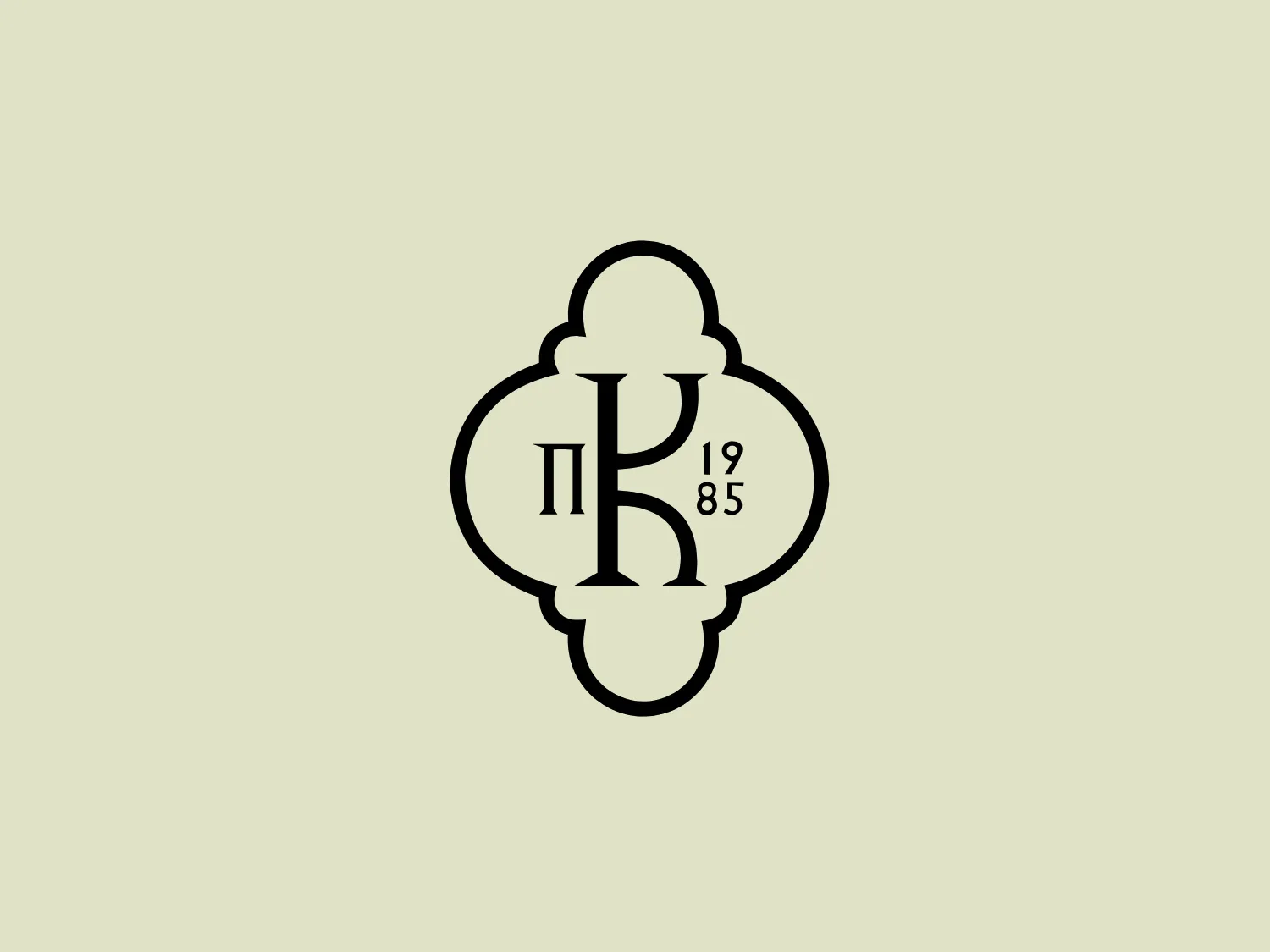 The Karipidis Estate logo features a bold, black monogram within an ornate frame that has a classic, symmetric quatrefoil shape, somewhat reminiscent of a clover or a cross with rounded edges. The monogram employs a serif font for the two primary letters, which are prominently displayed in the center, suggesting a sense of tradition and sophistication. A smaller serif typeface is used for the year "1985," which is positioned below the letters, adding a historical note to the design. The overall aesthetic of the Karipidis Estate logo is elegant and timeless, appropriate for an established brand or institution that values heritage. Given the classical and clean design, a subtle and soft background color would complement it well.