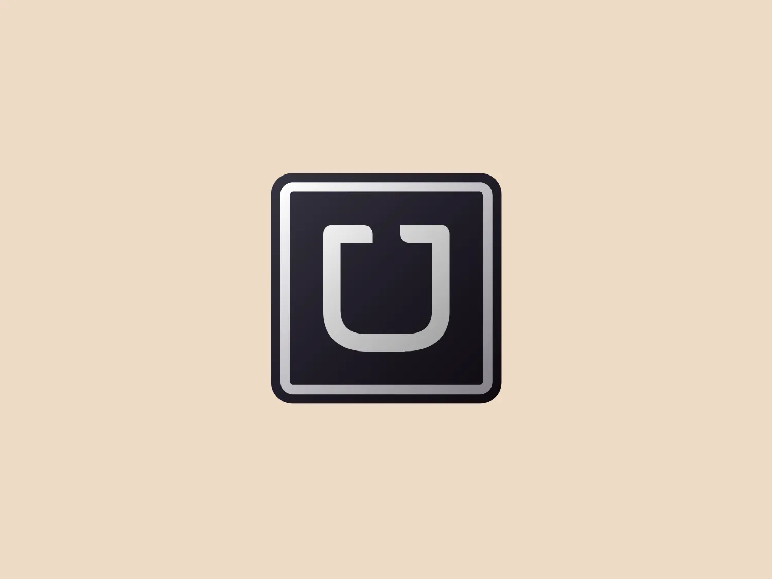 The Uber logo boasts a minimalist design, showcasing a bold, solid letter "U" at the center of a square with rounded corners. The modern, geometric style of the "U" features softened edges and is colored in a deep shade of gray or black, creating a stark contrast against the lighter grayish-silver background of the square. The monochromatic color scheme and sleek, professional aesthetic make for a versatile and contemporary emblem.