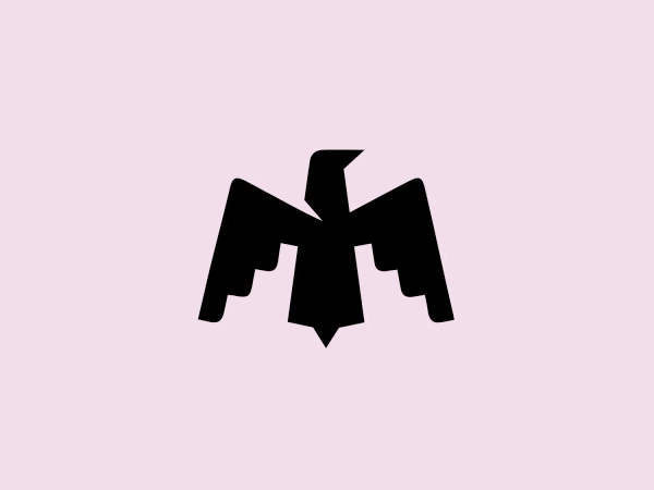 The Maha Festival logo is a stylized, abstract design resembling a bird in flight viewed from the front, with its wings outstretched. The aesthetic is modern and minimalistic, composed of solid, geometric shapes that give it a bold and dynamic feel. The entirely black color provides high contrast and would stand out well against a lighter, softer background. An interesting feature is the negative space in the center, which forms what can be perceived as the bird's head and beak, pointing upwards.